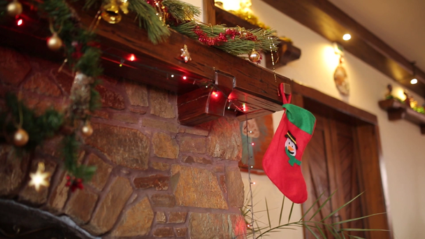 Warm cozy stone fireplace decorated for Christmas with wreath, stockings, garland lights. Mantelpiece with decorations for New Year holidays. Authentic festive interior decor. Dolly shot. - Footage, Video