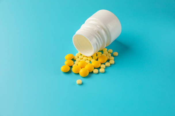 Yellow pills and plastic white bottle. Blue background with copy space for text. - Photo, Image