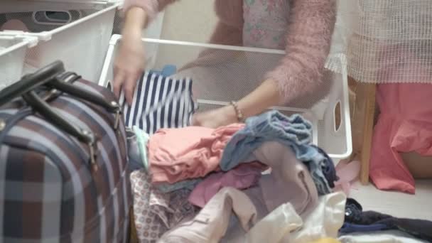 Una hermosa niña, una joven madre recoge y dobla la ropa de los niños en cestas en su vestidor. pone las cosas en orden
 - Imágenes, Vídeo