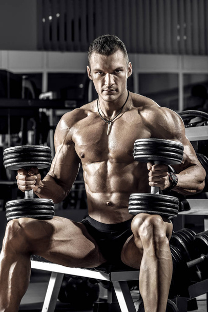 guy bodybuilder, perform exercise with dumbbell, in dark gym - Фото, зображення