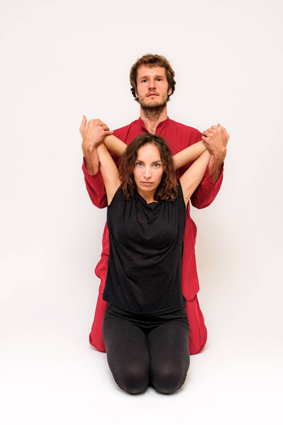 Photo of yoga poses on the floor for two stretching and relaxing on a white background. The man stretches the woman right in front of the camera. - Foto, imagen