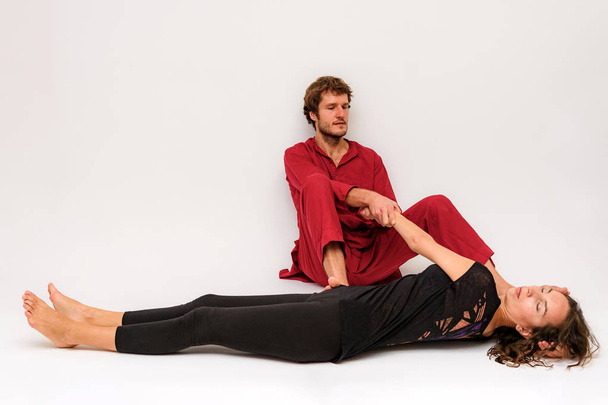 Photo of yoga poses on the floor for two stretching and relaxing on a white background. The man stretches the woman right in front of the camera. - Valokuva, kuva