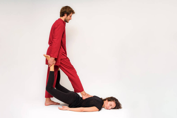 Photo of yoga poses on the floor for two stretching and relaxing on a white background. The man stretches the woman right in front of the camera. - Fotografie, Obrázek