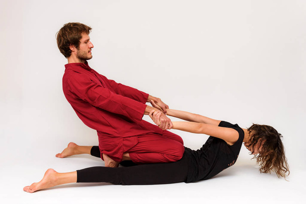 Photo of yoga poses on the floor for two stretching and relaxing on a white background. The man stretches the woman right in front of the camera. - Фото, изображение