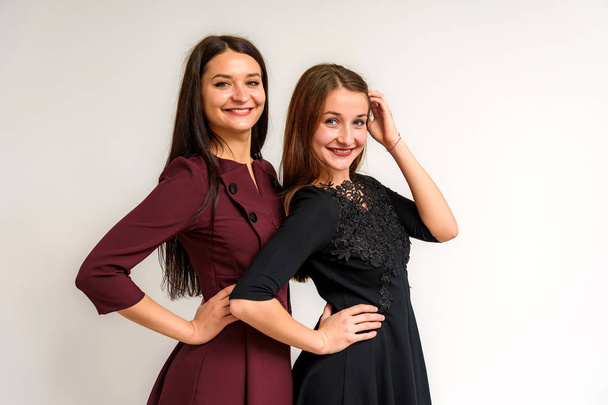 Studio muotokuva kaunis brunette tytöt sisaret valkoisella taustalla mekko erilaisia tunteita. He seisovat kameran edessä hymyillen ja näyttäen onnellisilta.
. - Valokuva, kuva