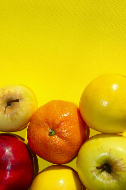 黄色の背景にカラフルな果物。マンダリン、レモン、黄色の背景でアップル。健康食品のコンセプト. - 写真・画像