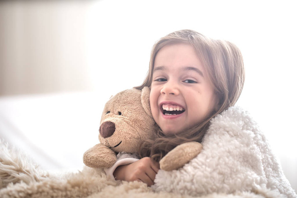 Маленькая красивая милая девочка обнимает игрушку медвежонка Тедди на светлом фоне, место для текста
 - Фото, изображение