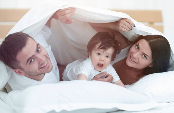 Happy family posing under a duvet while looking at the camera - Φωτογραφία, εικόνα