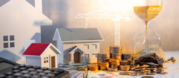 Real estate or property development. Construction business investment concept. Home mortgage loan rate. Coin stack on international banknotes with calculator, house and crane models on the table. - Photo, Image