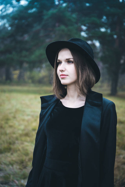 Portrait of a girl in a black hat in the gloomy forest - Foto, imagen