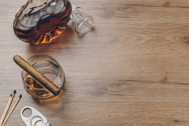 Sigaro cubano su un bicchiere di whisky bourbon, un decanter di whisky con un tagliasigari in acciaio inox e fiammiferi sul tavolo di legno
 - Foto, immagini