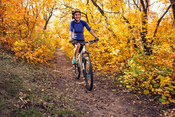 The girl with a backpack rides a bike in the autumn park. Slender woman trains in nature. Sports in the forest. Tourist rides on a dirt trail. Traveling by bike. - Fotoğraf, Görsel