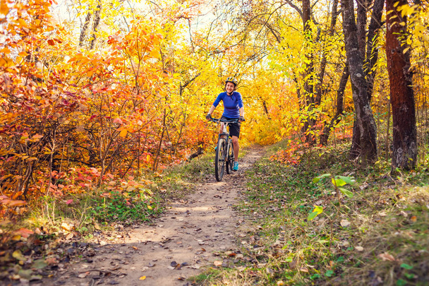 Ciclismo en el bosque. Chica monta en bicicleta en un sendero forestal. Mujer montando su bicicleta en el parque. Recorrido en bicicleta. Viaja a lugares pintorescos. Árboles de otoño
. - Foto, imagen