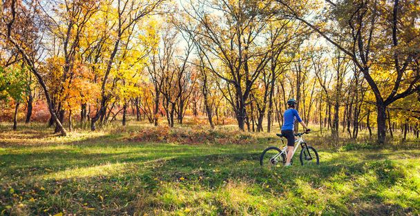 Das Mädchen mit dem Rucksack radelt im Herbstpark. Die schlanke Frau trainiert in der Natur. Sport im Wald. Ausritte auf einem Feldweg. Mit dem Fahrrad unterwegs. - Foto, Bild