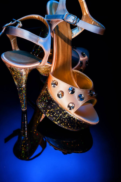 High-heeled shoes for dancing and striptease stand on a glass reflective surface. Champagne-colored shoes with round stones. - Foto, Bild