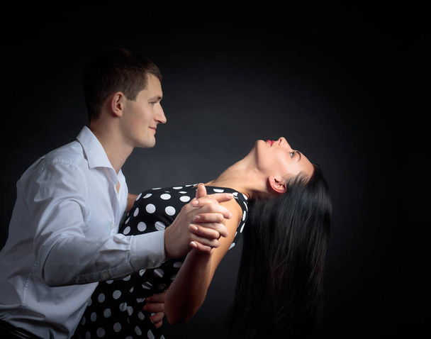 水玉ドレスと白いシャツを着たタンゴを踊る男性の若い美しい女性。スタジオでダンスの愛のカップル. - 写真・画像