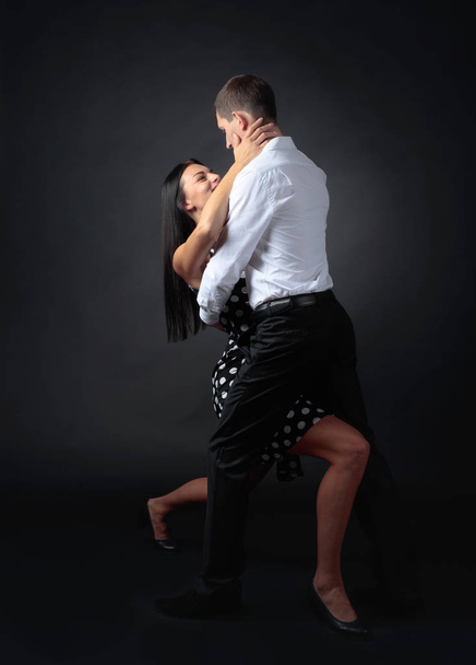 Young beautiful woman in polka dot dress and man in white shirt dancing tango. Couple in love dancing in the Studio. - Zdjęcie, obraz