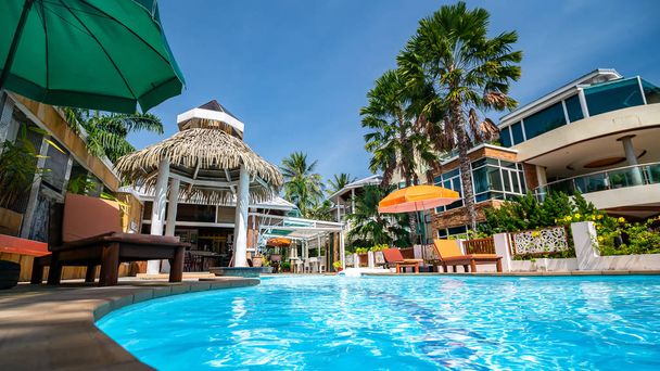 Piscina em resort de luxo ou hotel com vista para coqueiro e praia sob céu azul, Tailândia
 - Foto, Imagem