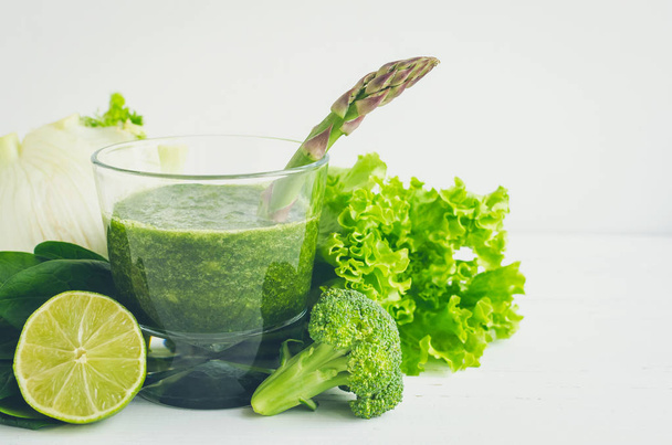 Detox green smoothie in a glass with ingredients: spinach, asparagus, lettuce, fennel, lime and broccoli on white wooden background. Dieting clean eating vegan healthy lifestyle concept. Copy space. - Foto, afbeelding