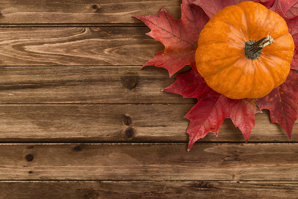 Pumpkin with red maple leafs disposed on wooden table. Flat lay, top view fall autumn concept. - Fotoğraf, Görsel