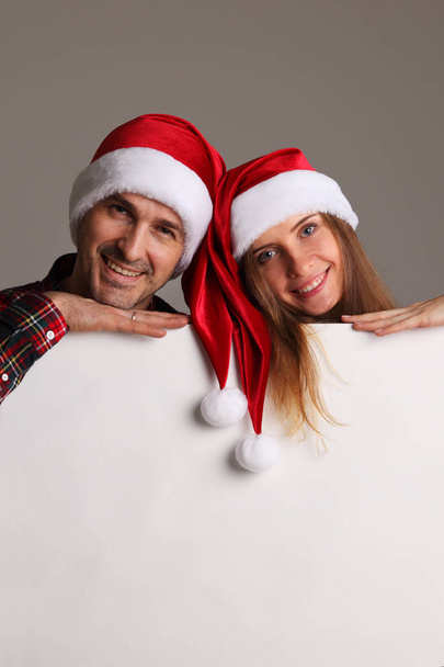 Happy couple in Santa hats holding blank banner with copy space - Photo, Image