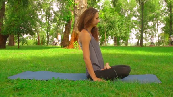 Mädchen sitzt auf der blauen Yogamatte und trainiert im Park - Filmmaterial, Video