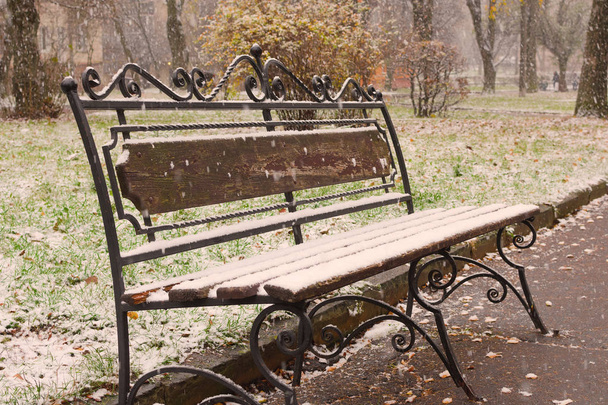 Jesienne dekoracje: Stary ogród ława w późnym upadku objętych pierwszym śniegiem. Strzelać w październiku. - Zdjęcie, obraz