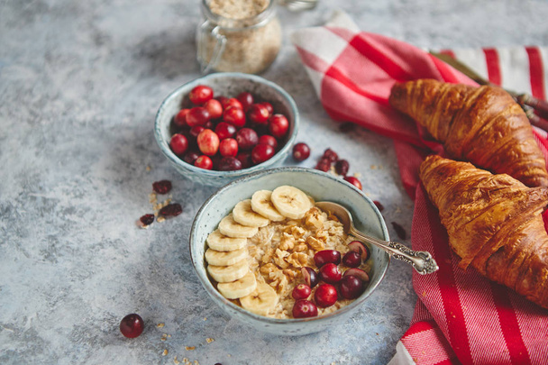 Ceramic bowl of oatmeal porridge with banana, fresh cranberries and walnuts - Foto, Bild