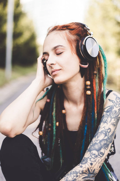 young girl with tattoo and dreadlocks listening to music in the park - Foto, Bild