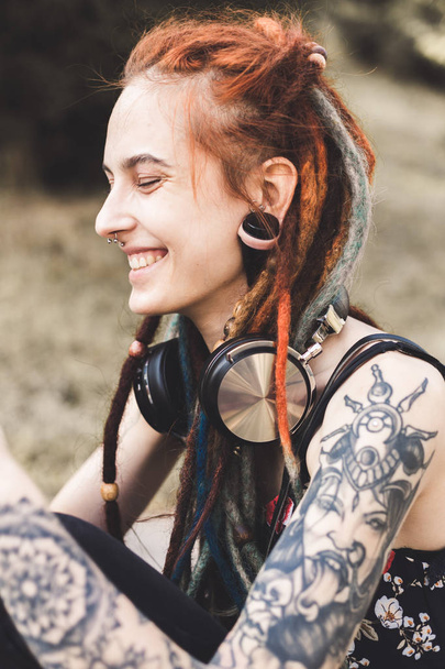 young girl with tattoo and dreadlocks listening to music in the park - Foto, Imagem