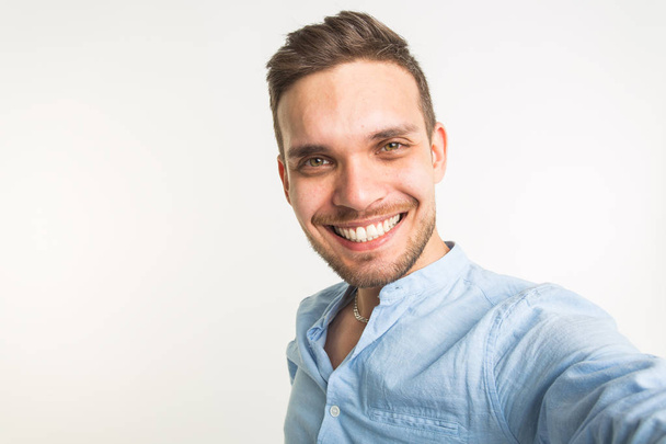 Fashion and people concept - handsome man make a selfie photo and smiling on white background - Fotografie, Obrázek