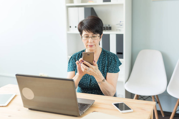 Conceito de negócios, pessoas e tecnologia - mulher de negócios confiante usando seu smartphone enquanto trabalha
 - Foto, Imagem