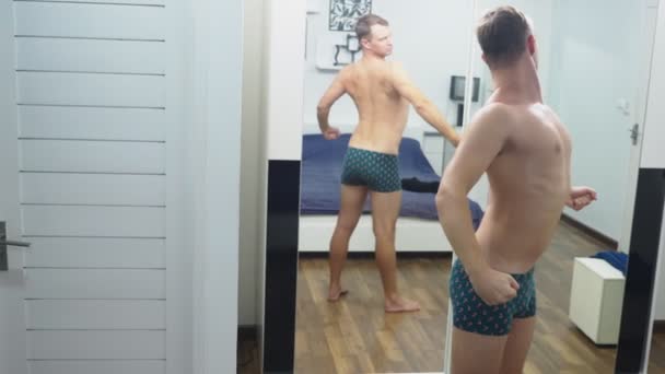 Young man checking his muscles in front of a mirror in the bedroom - Video, Çekim
