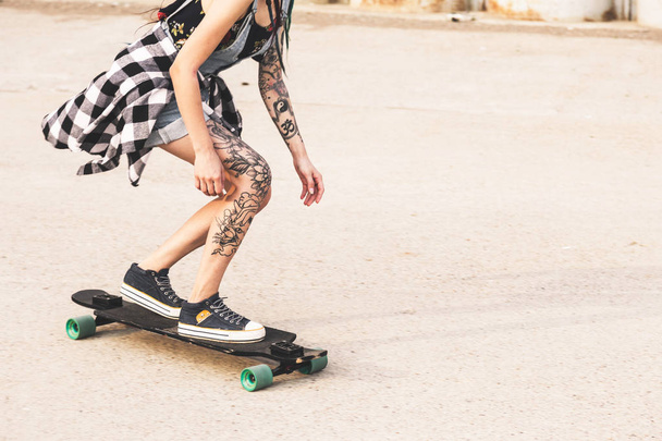 young girl with tattoo rides on a longboard - Zdjęcie, obraz