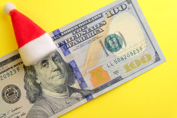 Chapeau rouge du Père Noël sur la tête de Franklin sur cent dollars. Combien d'argent les gens dépensent-ils pendant les vacances d'hiver ? Dans la nouvelle année sans dette financière. Fond jaune
. - Photo, image