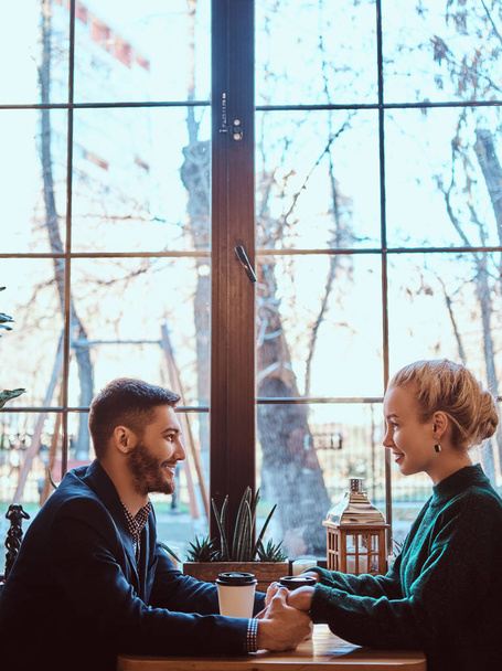Attractive young couple holding hands, looking at each other and talking while sitting in the restaurant. - Foto, immagini