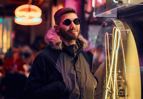 Yakışıklı bir adam sokakta gece ayakta ceplerinde bir ceket ve elleri ile güneş gözlüğü giyiyor.  - Fotoğraf, Görsel