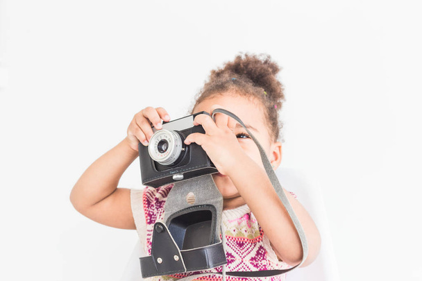 Портрет маленькой девочки в красочном платье, фотографирующей на старинную винтажную камеру
 - Фото, изображение