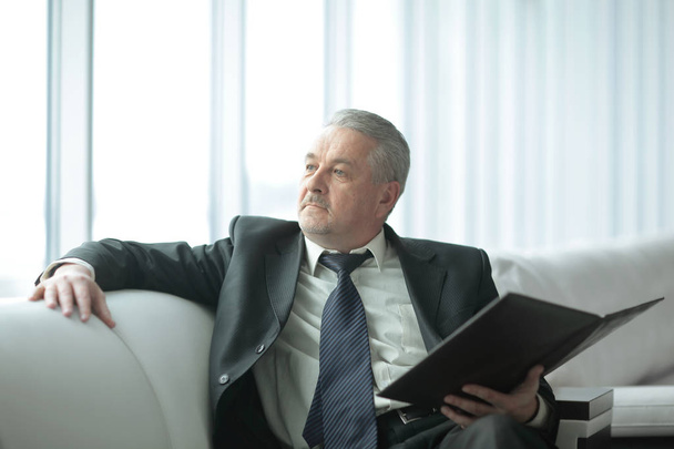 pensive businessman with clipboard sitting on the office couch - 写真・画像