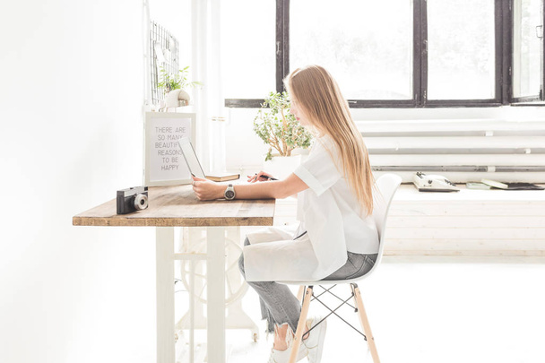 Joven mujer de negocios trabajando en casa detrás de un portátil. Espacio de trabajo de estilo escandinavo creativo
 - Foto, imagen