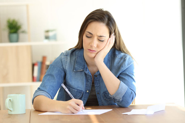 Front view of a worried woman writing notes or a letter at home - Photo, image