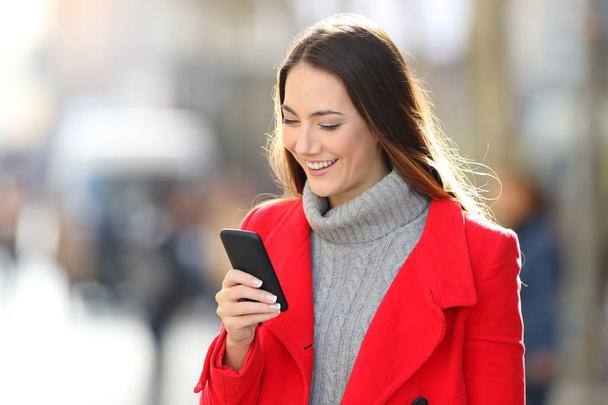 Felice signora in rosso utilizzando uno smartphone all'aperto in strada in inverno
 - Foto, immagini