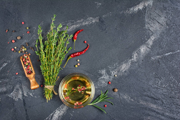 Aromatic or flavored olive oil in glass bowl with spices and herbs as chili peppers and thyme on black marble background with copy space - Zdjęcie, obraz