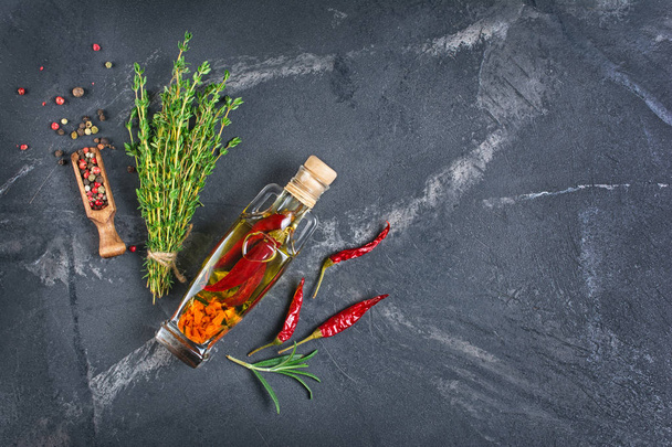 Aromatic or flavored olive oil in glass bottle with spices and herbs as chili peppers and thyme on black marble background with copy space - Photo, Image