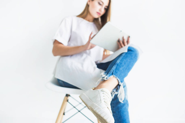 Portrait of a young stylish blonde girl in a white T-shirt and blue jeans using a tablet on a white background - Valokuva, kuva