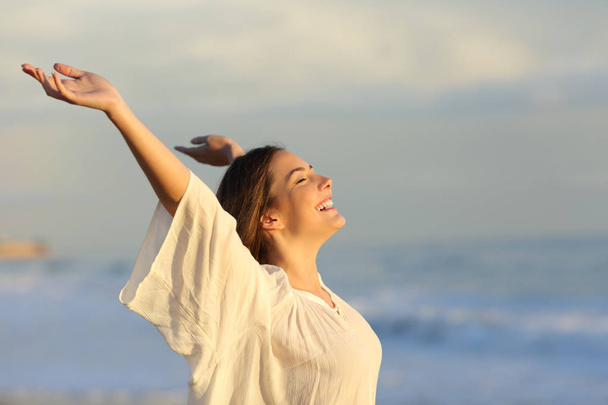 Joyful woman enjoying a day on the beach raising arms at sunset - 写真・画像