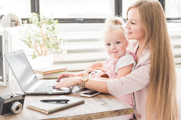 ノート パソコンの後ろに小さな子供と一緒に家で働く若いビジネス女性。北欧スタイルの創造的なワークスペースです。出産で仕事を残してください。 - 写真・画像