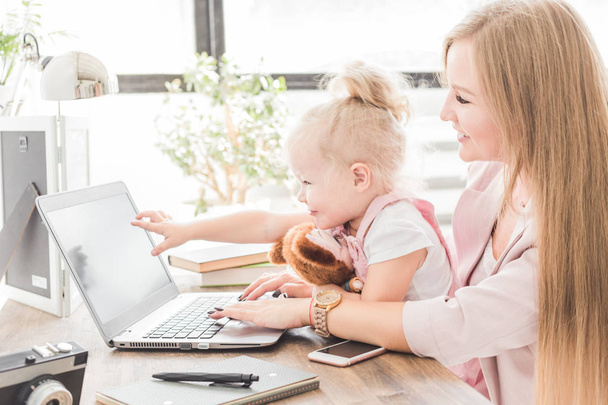 Young business woman working at home behind the laptop with a little child. Creative Scandinavian style workspace. Work on maternity leave - Photo, image