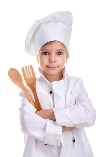 Smirking dziewczyna kucharzem biały uniform izolowana na białym tle. Holding drewnianą łyżką i widelcem w założonymi rękoma. Obraz portret - Zdjęcie, obraz