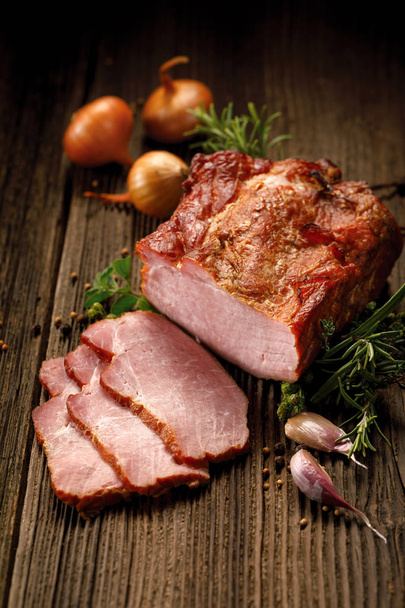 Carnes defumadas, lombo de porco defumado fatiado em uma mesa de madeira com adição de ervas frescas e especiarias aromáticas
.   - Foto, Imagem